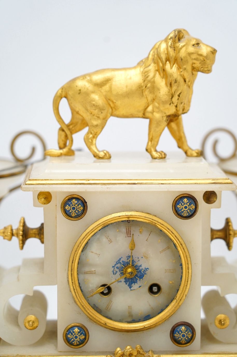 An early 20th century alabaster and gilt metal clock garniture with enamel panels, surmounted with a lion, with pendulum, no key, clock 30cm high. Condition - poor